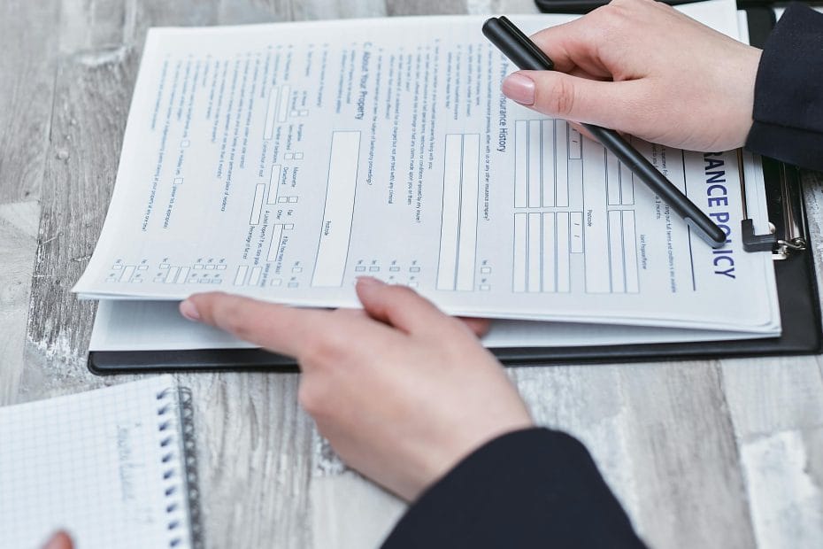 Close-up of hands analyzing insurance policy paperwork with pen on table.