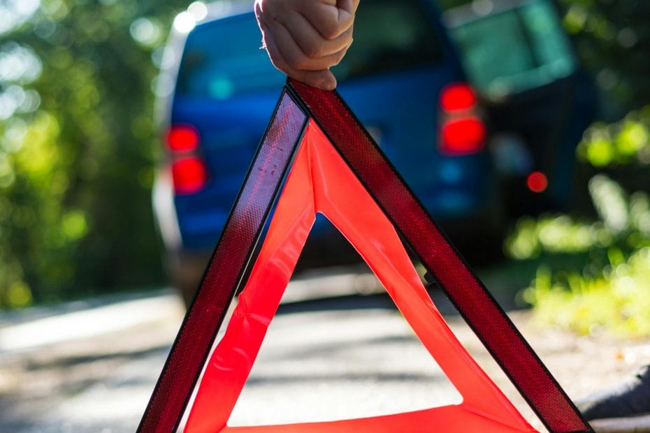 Close-up of a hand placing an emergency warning triangle by a car.